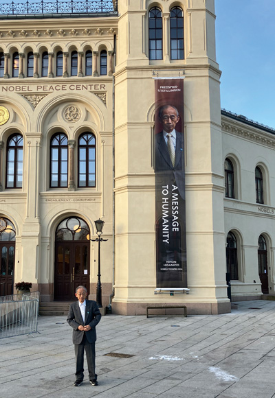 オスロ市内で自身の写真入り垂れ幕の前に立つ濱住さん